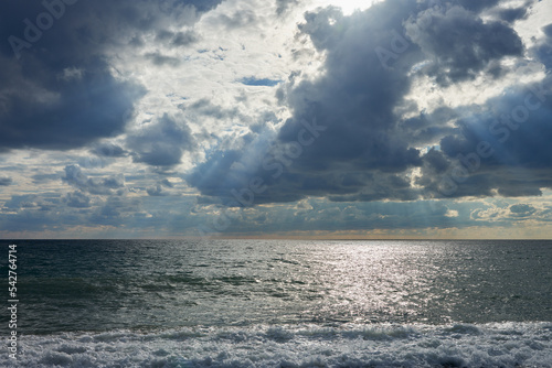 Sea. Bad weather. Rare sun rays break through heavy leaden clouds. The reflection of sunlight on the water. Copy space.