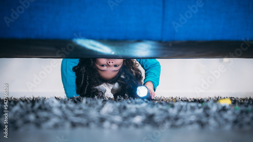 A little girl is looking for something under the bed in bedroom. photo