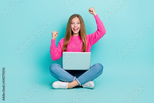 Photo of cheerful overjoyed lady sit floor raise hands fists rejoice successful pass test lesson exam isolated on cyan color background © deagreez