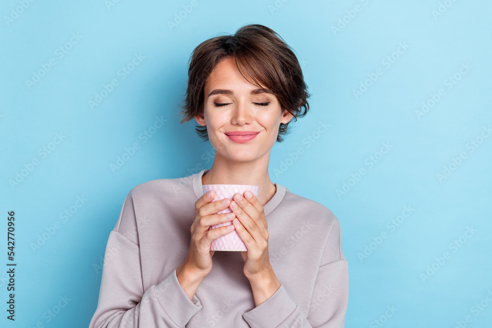 Photo of pretty cute satisfied lady dressed stylish outfit eyes closed hold hot tea enjoy isolated on blue color background Photo of pretty cute satisfied lady dressed stylish outfit eyes closed hold hot tea enjoy isolated on blue color background