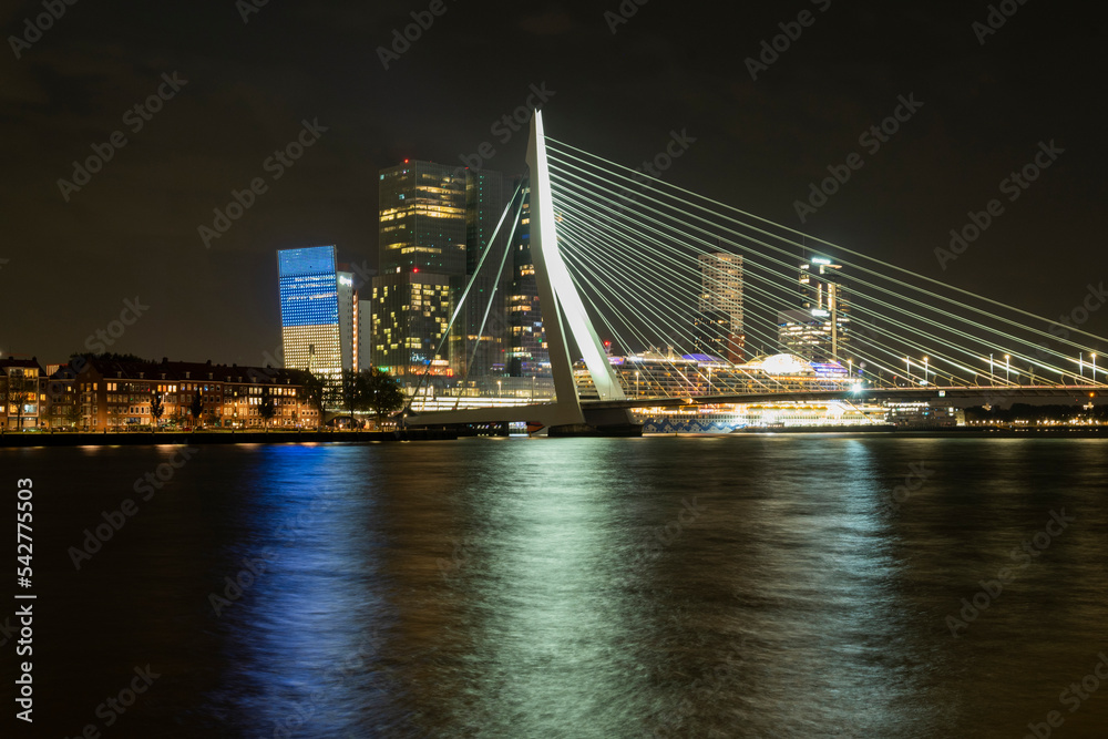 Erasmusbrug cable-stayed bridge over the Maas river in the center of Rotterdam with city view and reflection at night