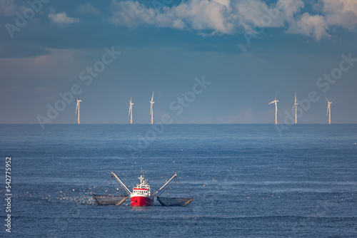 A cutter with lifted drag nets on the North sea with wind turbines in the background photo