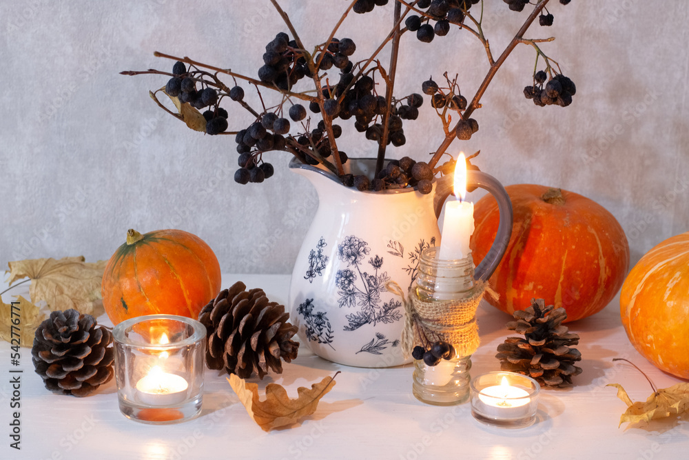 Autumn decoration on dresser. Branches of chokeberry in vase, pumpkins, cones and candles.