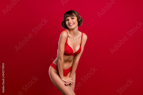 Portrait of attractive cheerful alluring slim shy girl posing wearing ligerie isolated over bright red color background
