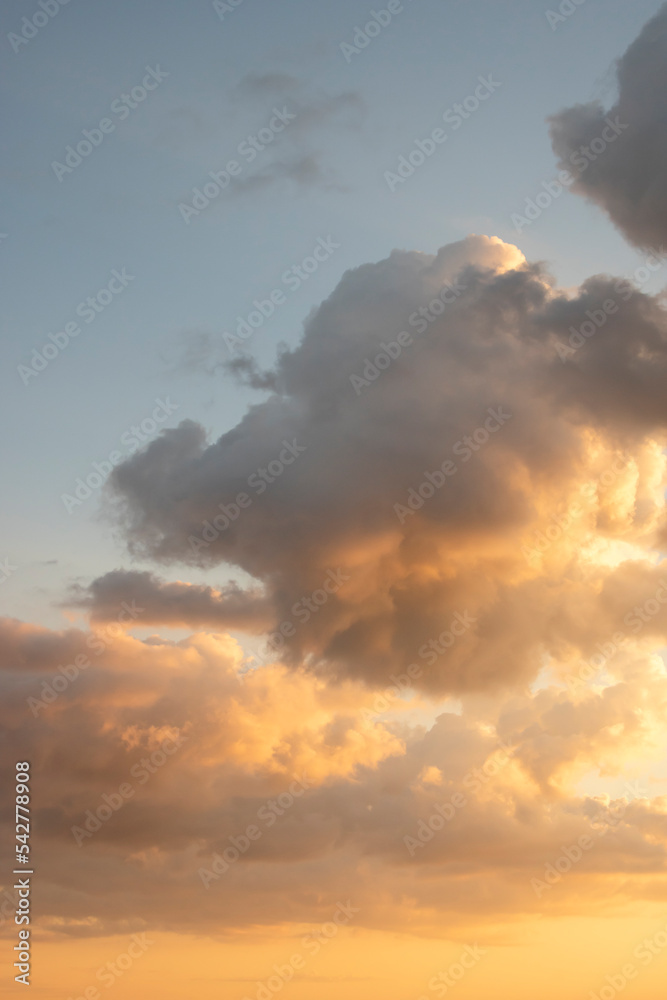 Sunset landscape with puffy clouds lit by orange setting sun and blue,  teal sky. Dramatic orange clouds