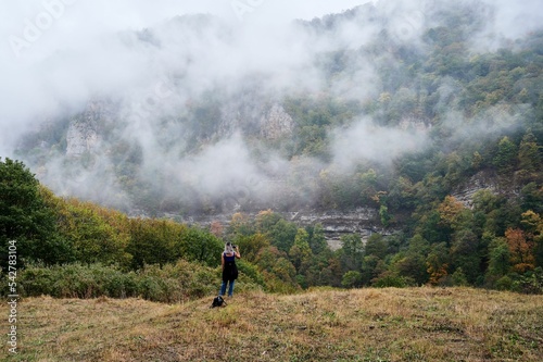 Woman in a field in front of a rocky mountain and colorful trees coated in the mist photo