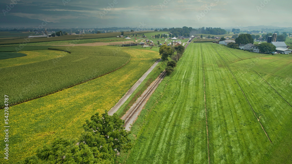 Drone View of Amish Countryside With Barns and Silos and a Single Railroad Track Traveling Through It, on Sunny Day.