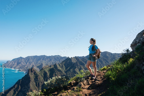 A girl hiker with a backpack goes on a hike in the Anaga Mountains watching beautiful costal scenery. - Tenerife, Canary Islands, Spain. coast view photo