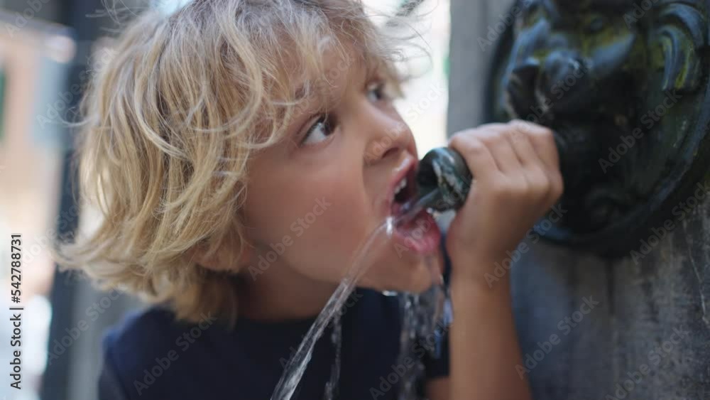 One blond child drinking from public water fountain. Kid drinks from urban street faucet One blond child drinking from public water fountain. Kid drinks from urban street faucet