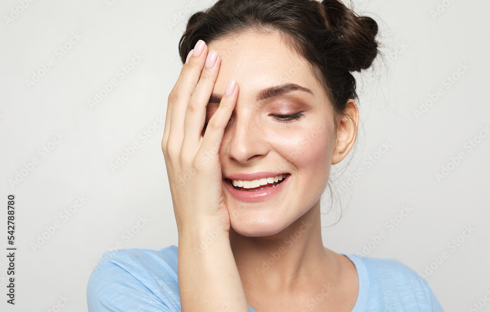 A beautiful young woman with dark hair in a blue t-shirt covers her eye with her palm and laughs. A beautiful young woman with dark hair in a blue t-shirt covers her eye with her palm and laughs.