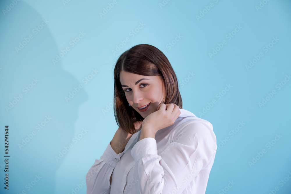 Close-up portrait of beautiful smiling caucasian woman with brown hair wearing white shirt and holding collar. Blue background. Selective focus. People theme. Close-up portrait of beautiful smiling caucasian woman with brown hair wearing white shirt and holding collar. Blue background. Selective focus. People theme.