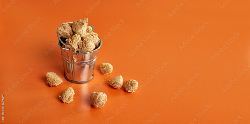 Textured pieces of soy flour in a small bucket on an orange background. Textured pieces of soy flour in a small bucket on an orange background.