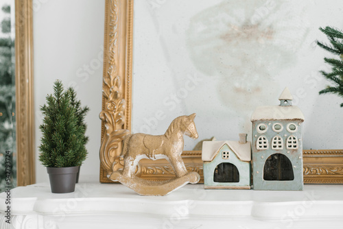 Winter holiday home decor on the fireplace: a horse, a potted Christmas tree, fabulous souvenir houses. Christmas Room Decoration