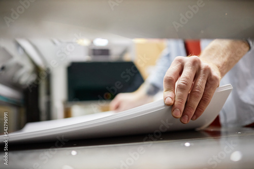 Close up of man putting stack of paper in printing machine at publishing shop, copy space photo