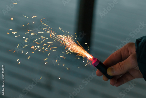 Burning Firecracker with Sparks. Guy Holding a Petard in a Hand. Loud and Dangerous New Year's Entertainment. Hooliganism with Pyrotechnics. Noise of Firecrackers in Public Places photo