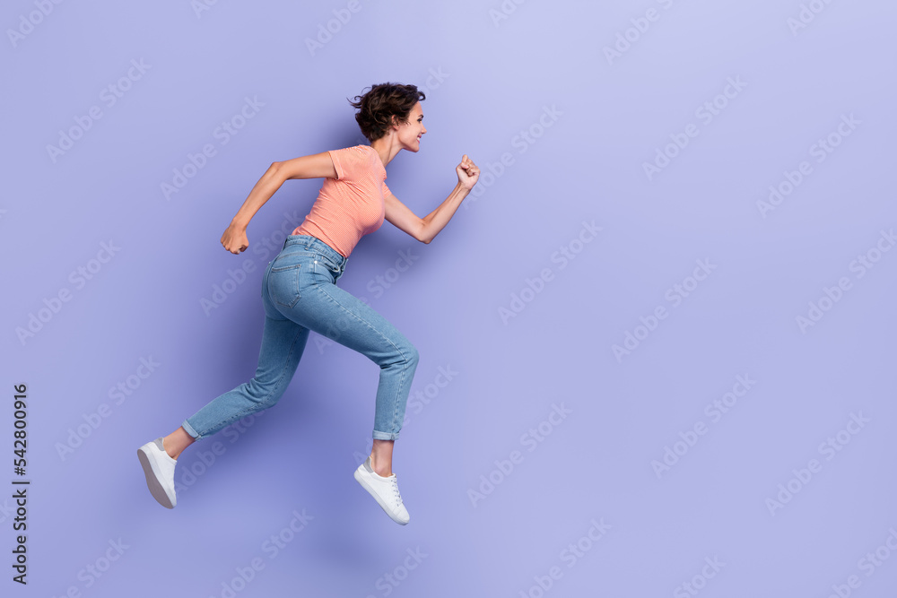 Full length photo of sweet shiny girl dressed orange t-shirt jumping high running fast empty space isolated purple color background Full length photo of sweet shiny girl dressed orange t-shirt jumping high running fast empty space isolated purple color background