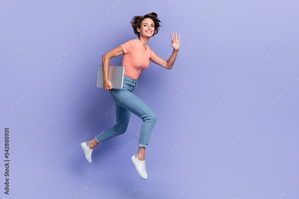 Full length photo of pretty sweet girl dressed orange t-shirt jumping holding modern gadget empty space isolated purple color background