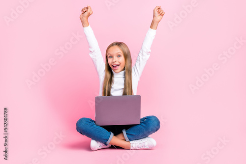 Full body photo of excited delighted person sit floor use netbook raise fists achievement isolated on pink color background