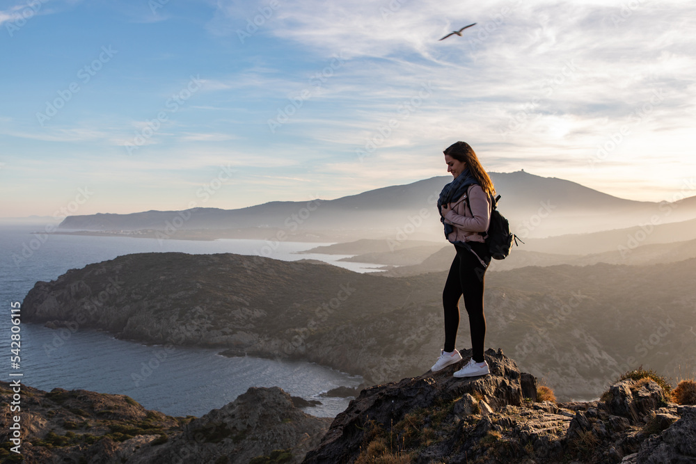 Beautiful women standing on a cliff during sunset with the sea on the background Beautiful women standing on a cliff during sunset with the sea on the background