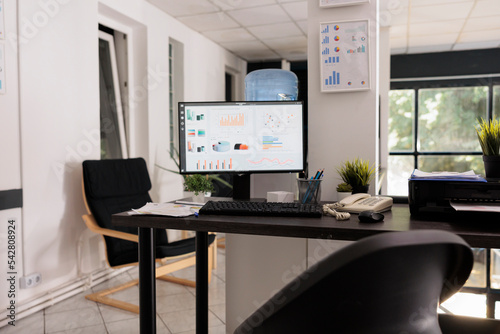 Empty office at the beginning of the day with growth statistics reflected on desktop monitor. Annual projections hanging on wall in workplace with no people during daytime.