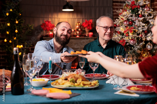 Family having christmas dinner together  eating traditional food at festive table  man passing woman plate with dish. People gathering with parents on winter holidays  celebrating xmas