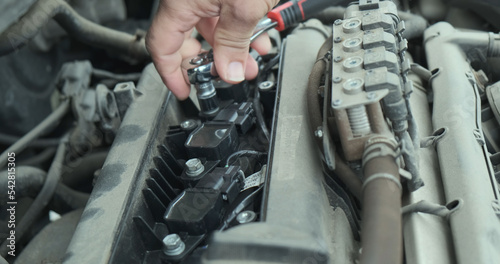 Men's hands unscrew the bolts of the car's candle box under the hood with a ratchet wrench. Close-up. The concept of replacing candles in a car.