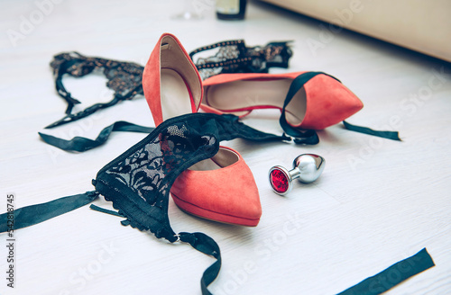 Beautiful black lingerie on the floor near the bed in the room with high-heeled shoes and anal plug. Quick sex concept.