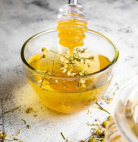 Yellow Sicilian lemon tea with spilled bee honey and chamomile on branch and flower. Mention health care, alternative medicine with fruits, herbs and plants, treatment of diseases and symptoms.