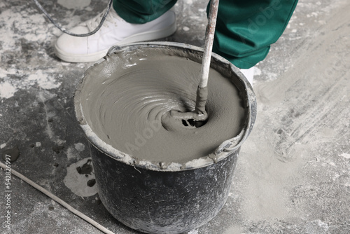 Worker mixing concrete in bucket indoors, closeup