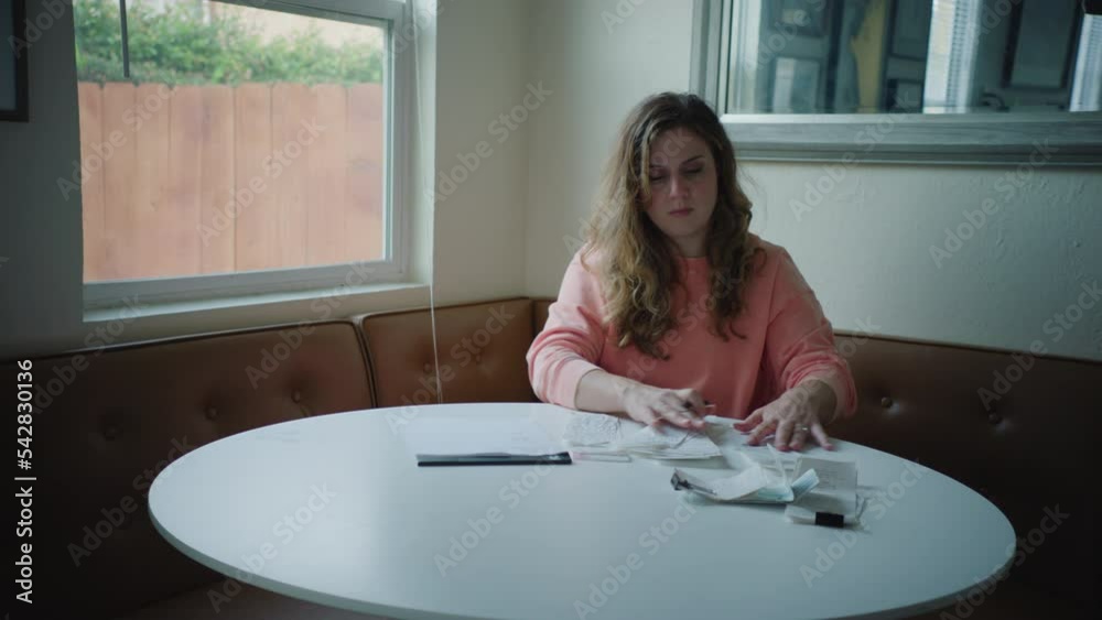 Handheld Shot of Woman Organizing Receipts on Corner Kitchen Table By Window, Wearing Pink Sweater Handheld Shot of Woman Organizing Receipts on Corner Kitchen Table By Window, Wearing Pink Sweater