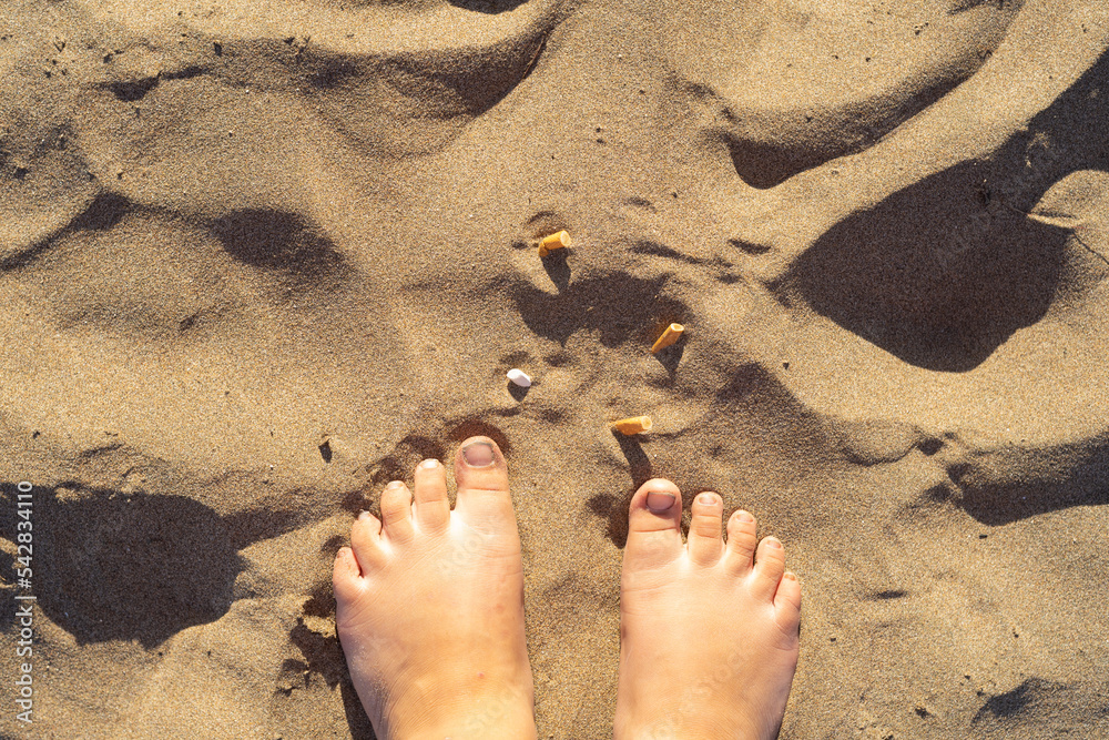 girl's feet on the beach with garbage contamination, plastics, bags and