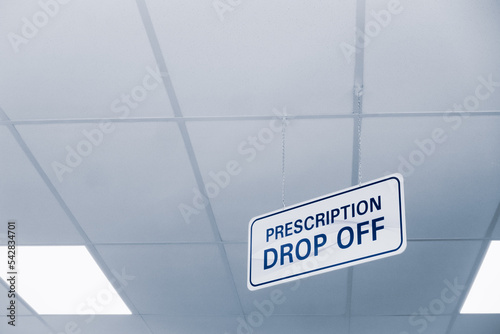 Plain white and blue prescription drop off sign hanging from a ceiling with copyspace inside a drugstore.