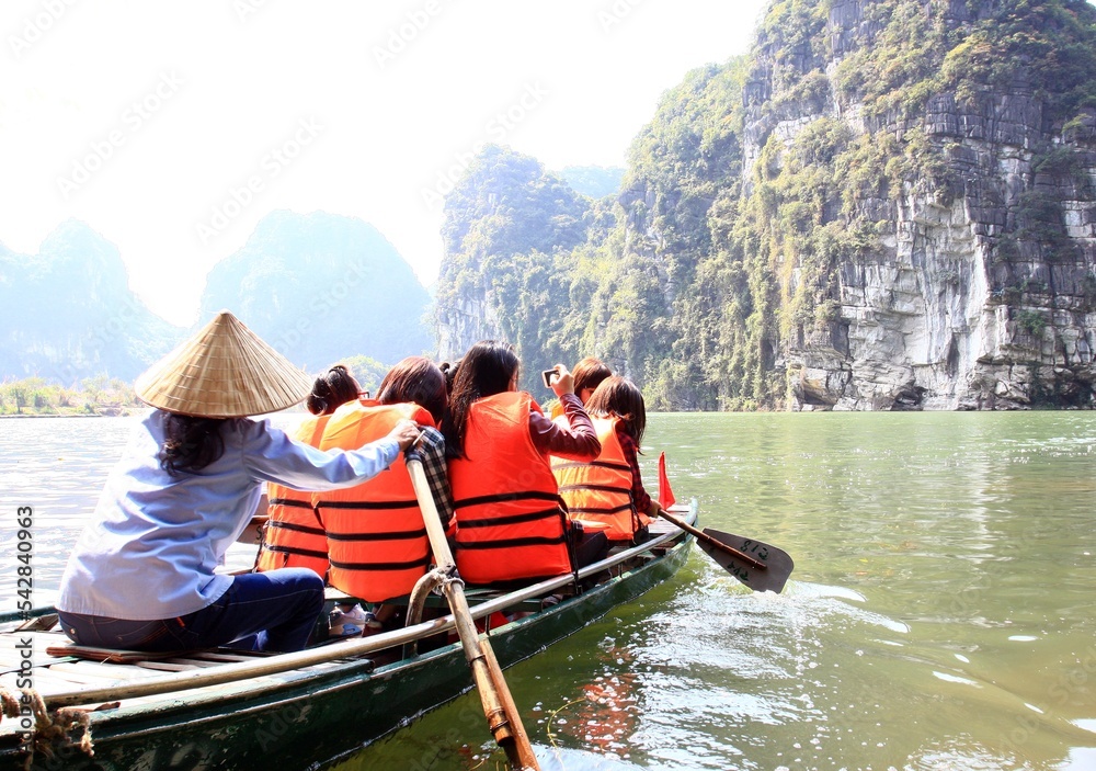 Tourists traveling in boat along the Ngo Dong River, Landscape formed by karst towers and rice fields, in Ninh Binh - Vietnam Tourists traveling in boat along the Ngo Dong River, Landscape formed by karst towers and rice fields, in Ninh Binh - Vietnam