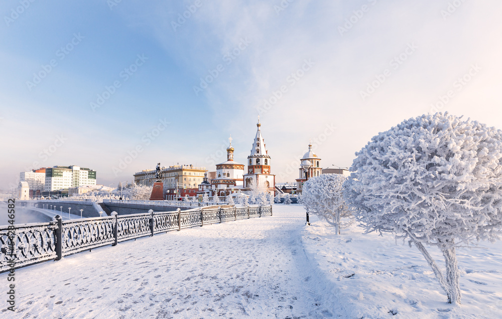 Obraz premium Irkutsk on frosty winter day. View from the snow-covered lower embankment of the Angara River to the Epiphany Cathedral and the monument to the founders of the city. Beautiful winter cityscape