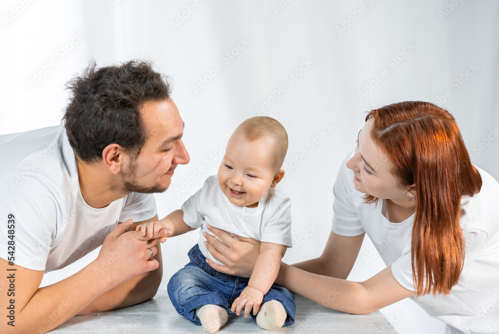 young parents lovingly look, play, kiss the child. white interior
