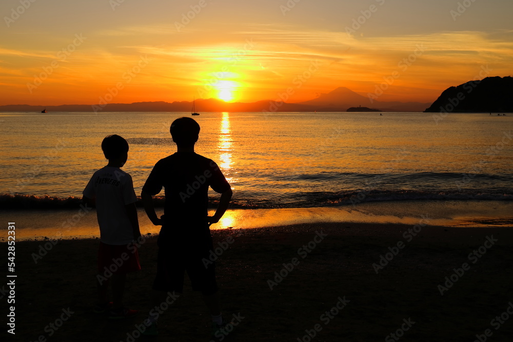 夕暮れの逗子海岸、波打ち際で夕陽を眺める兄弟の後ろ姿