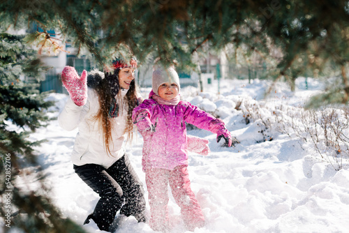 Caucasian woman and her little daughter hugging smiling having fun in sunny winter day. Horizontal headshot, side view. Blurred background. Happy parenting and winter activities concept.