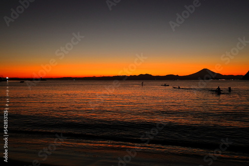夕暮れの逗子海岸、オレンジ色に染まる海でカヤックを楽しむ若者