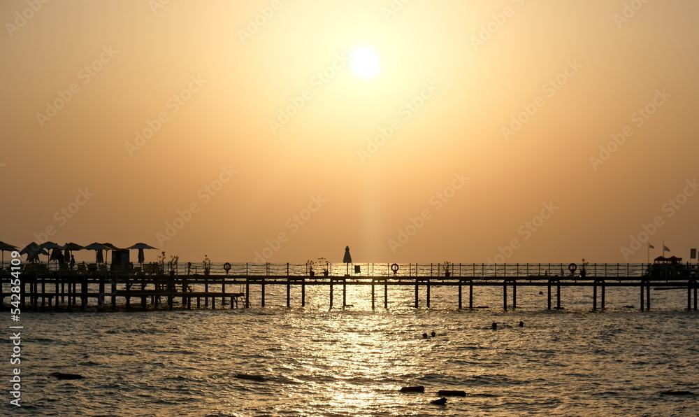 Pier on the background of the setting sun. Sea and sun, evening. Pier on the sea, Mediterranean sea