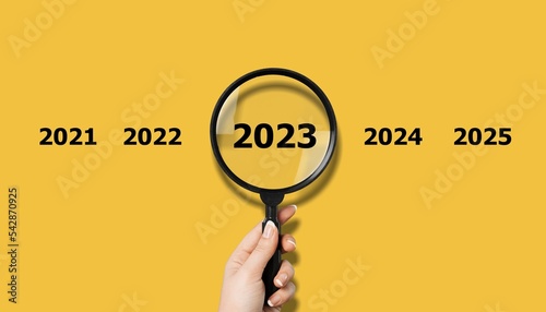 Human hand with magnifier and 2023 numbers