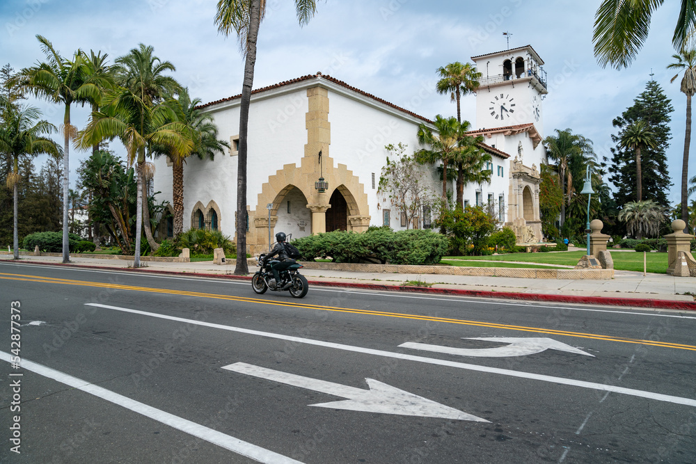 California, USA - May 20, 2018: exterior of Santa Barbara country courthouse with a male motorcyclist wearing black riding motorcycle by in spring. view from the other side of road