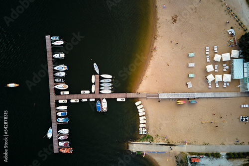 Aerial top view of boats and small jachts near wooden pier at the lake. Summer entertainment at water for tourists photo