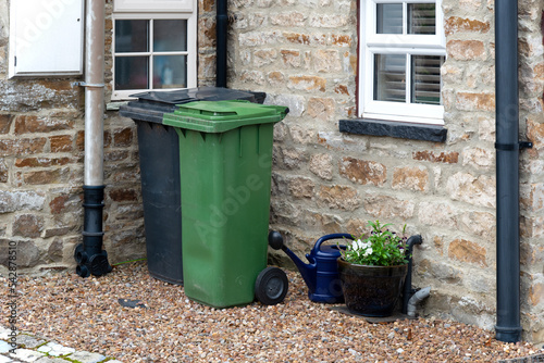 A Green and a black wheelie bin in front of a house entrance somewhere in a small village near Leyburn, Yorkshire, UK.