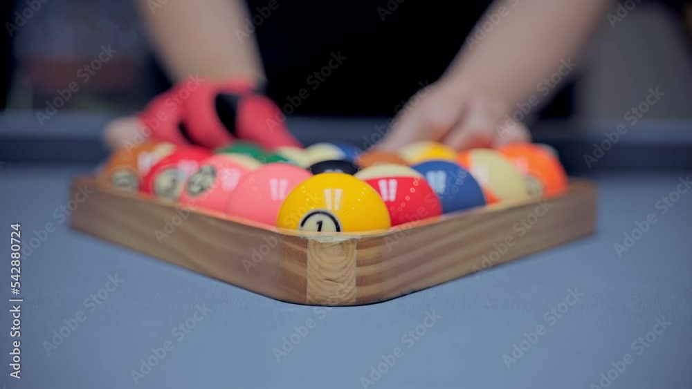 Billiard player's hands with gloves moves and levels the pyramid of balls. Play American pool. 15 colorful pool balls take part in the game. Classic blue baize table. Slow motion close up