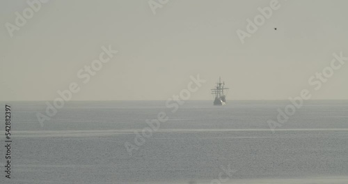 Ferdinand Magellan Nao Victoria carrack boat replica sails in the distance in the mediterranean at sunrise while a bird flies in calm sea in slow motion 60fps photo