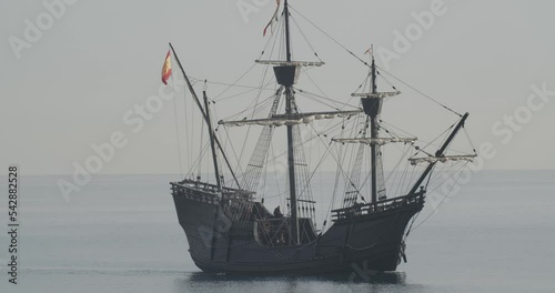 Ferdinand Magellan Nao Victoria carrack boat replica with spanish flag sails in the mediterranean at sunrise in calm sea side shot in slow motion 60fps photo
