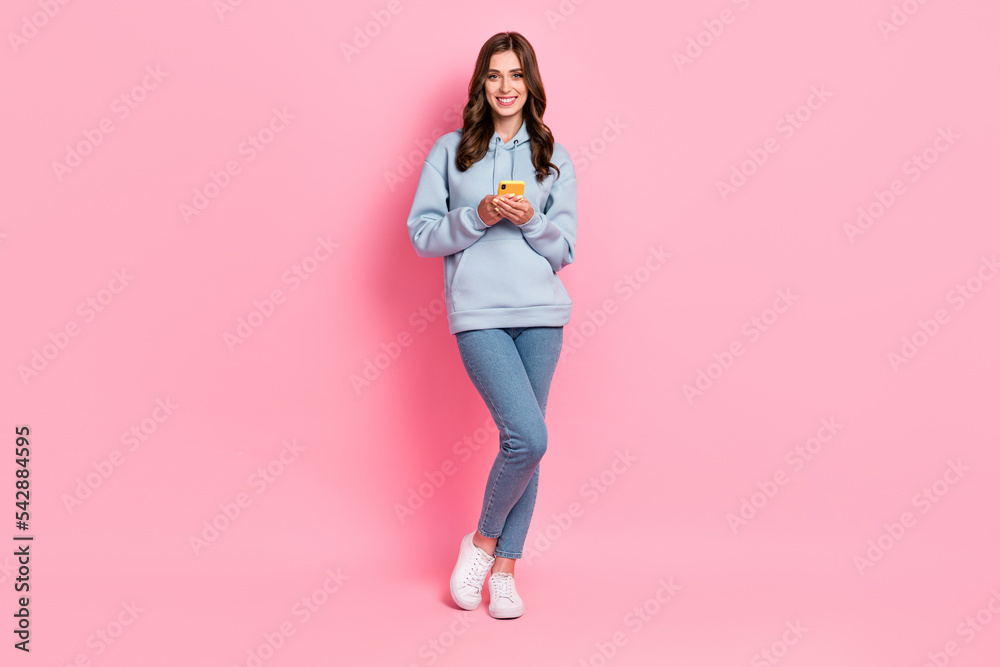 Full size photo of positive pretty girl hold use telephone toothy smile isolated on pink color background Full size photo of positive pretty girl hold use telephone toothy smile isolated on pink color background