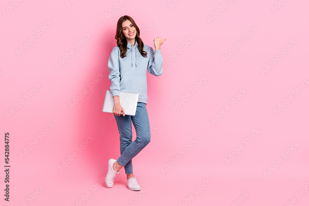 Full size photo of positive nice girl hold netbook direct thumb finger empty space isolated on pink color background Full size photo of positive nice girl hold netbook direct thumb finger empty space isolated on pink color background