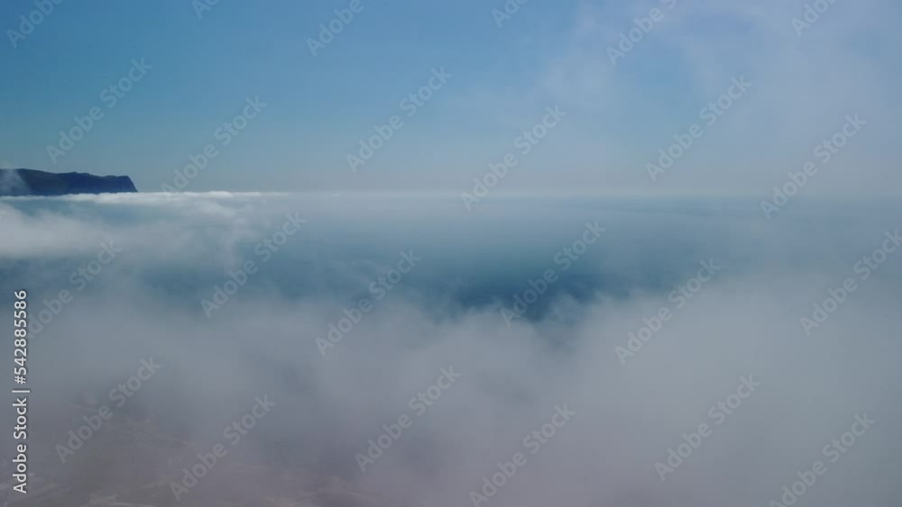 Aerial view. The drone flies over foggy and fluffy clouds. Blue sky sun and sea fog. Abstract aerial nature summer ocean sunset sea and sky background. Vacation, travel and holiday concept Aerial view. The drone flies over foggy and fluffy clouds. Blue sky sun and sea fog. Abstract aerial nature summer ocean sunset sea and sky background. Vacation, travel and holiday concept