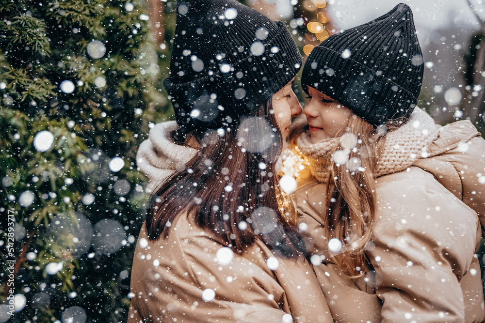 Obraz premium Winter holidays and people concept - happy morther and little daughter choosing christmas tree at street market. Happy family buys a Xmas tree.